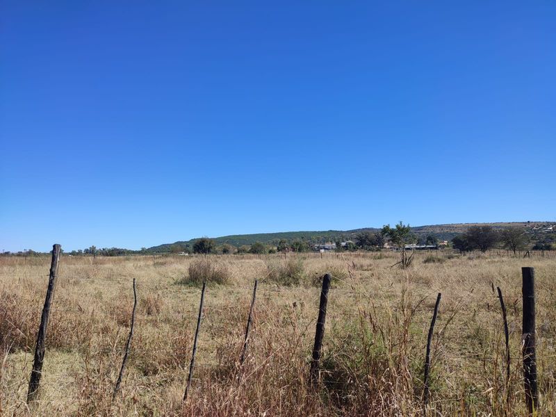 A view of a vacant residential plot featuring natural grass terrain and simple wire fencing with wooden posts.