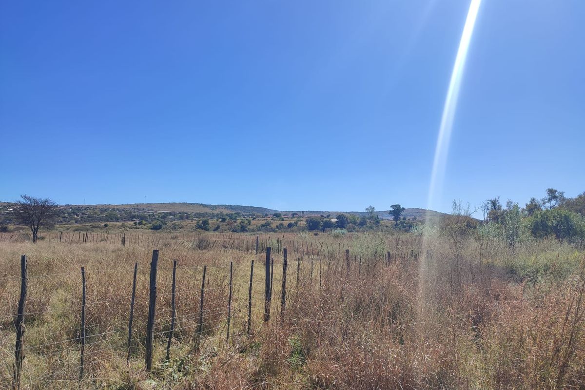 A wide-angle view of the vacant residential land featuring natural landscape, dry vegetation, and perimeter wire fencing with wooden posts.