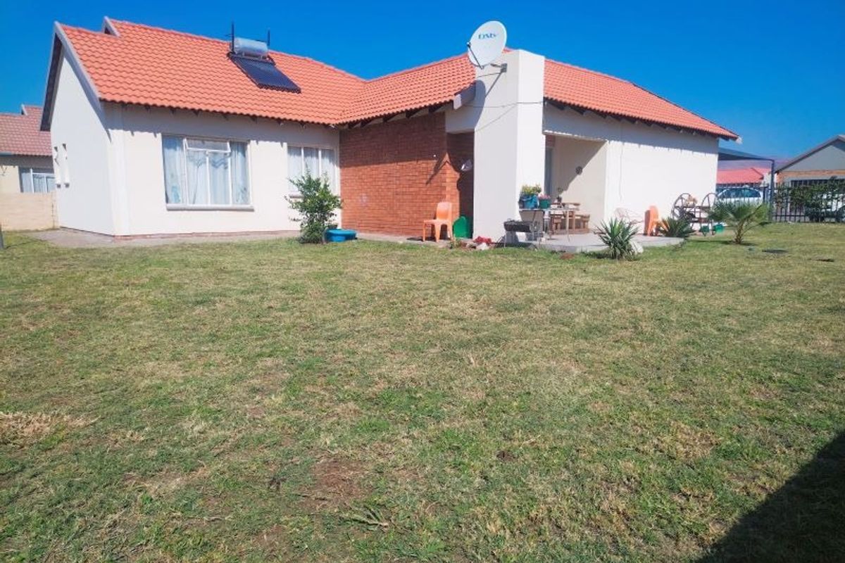 Rear view of the house featuring a spacious lawn, a covered patio area, and a solar water heating system installed on the tiled roof.