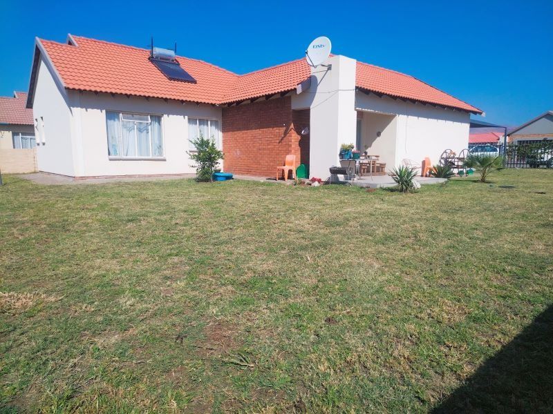 Rear view of the house featuring a spacious lawn, a covered patio area, and a solar water heating system installed on the tiled roof.