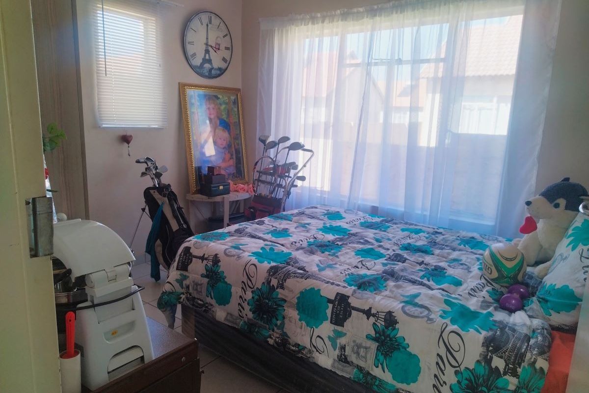 A functional bedroom featuring tiled flooring, a built-in cupboard, and large windows with venetian blinds, offering a bright and practical living space.