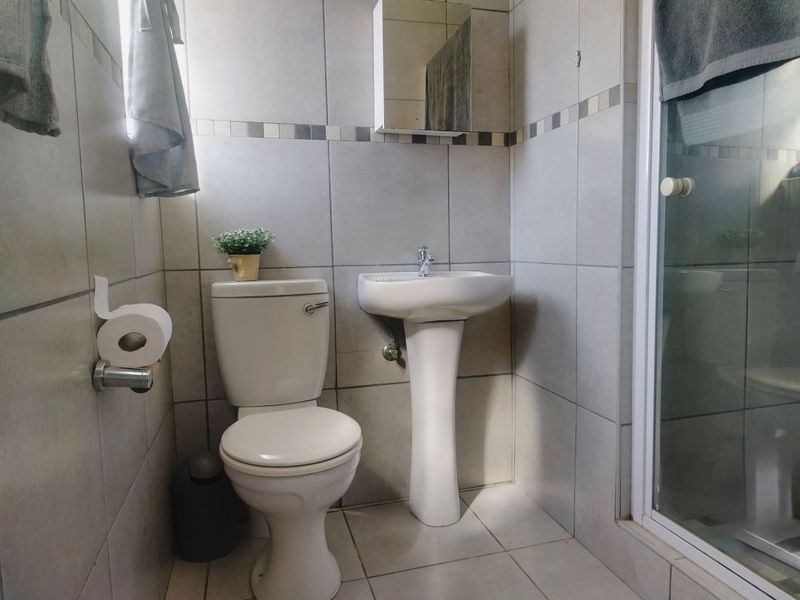 A functional bathroom featuring a pedestal sink, toilet, and a shower enclosure with neutral ceramic wall and floor tiling.