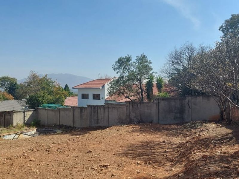 A vacant residential plot featuring a perimeter wall with electric fencing, showing natural terrain and surrounding neighborhood views.