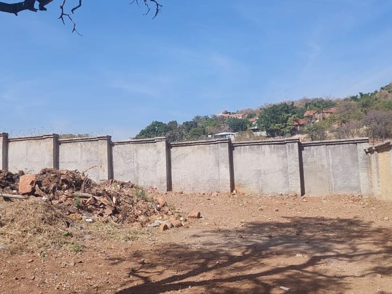 A vacant residential plot featuring a perimeter wall with security razor wire and an unlandscaped, uneven ground surface.