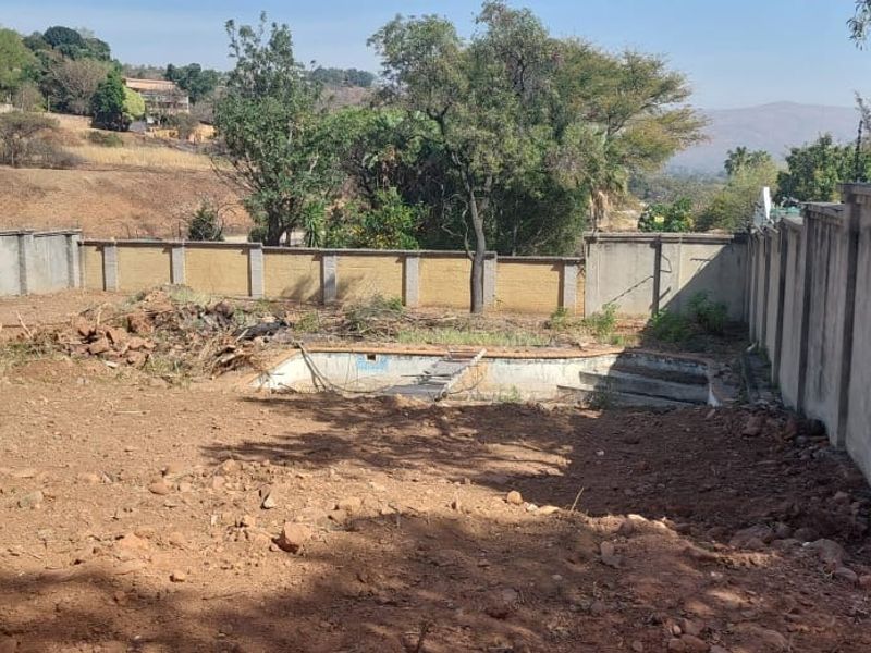 Vacant residential land featuring a derelict swimming pool and perimeter boundary walls, set against a natural landscape background.