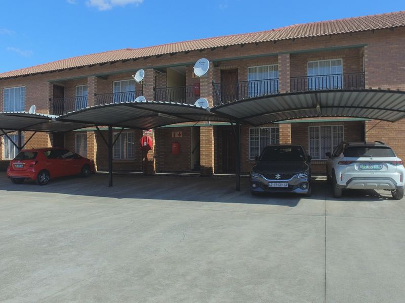 Exterior view of a multi-story brick apartment complex featuring covered parking bays and secure access points.