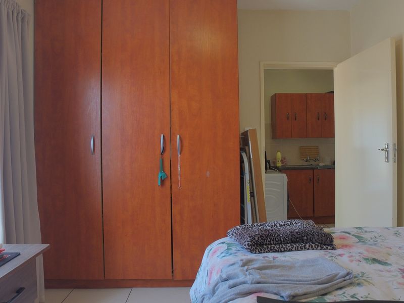 Bedroom featuring a large built-in wooden wardrobe and tiled flooring, with a view into an adjacent kitchen area.