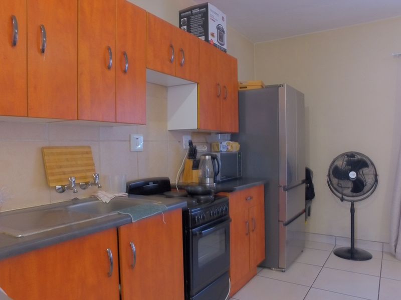 A functional kitchen featuring wood-look laminate cabinetry, a stainless steel sink, tiled backsplash, and a freestanding oven, with neutral tiled flooring throughout.