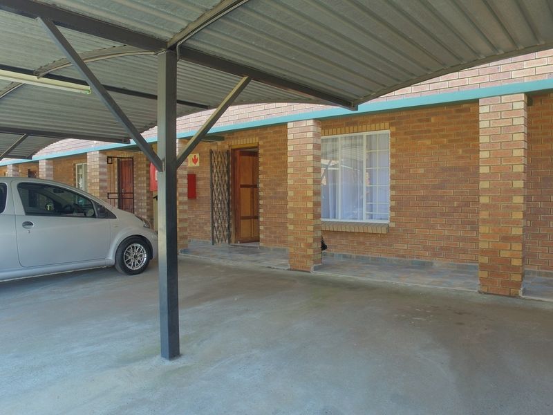 Exterior view of an apartment unit featuring a covered carport, brick facade, and a secure entrance with a security gate.