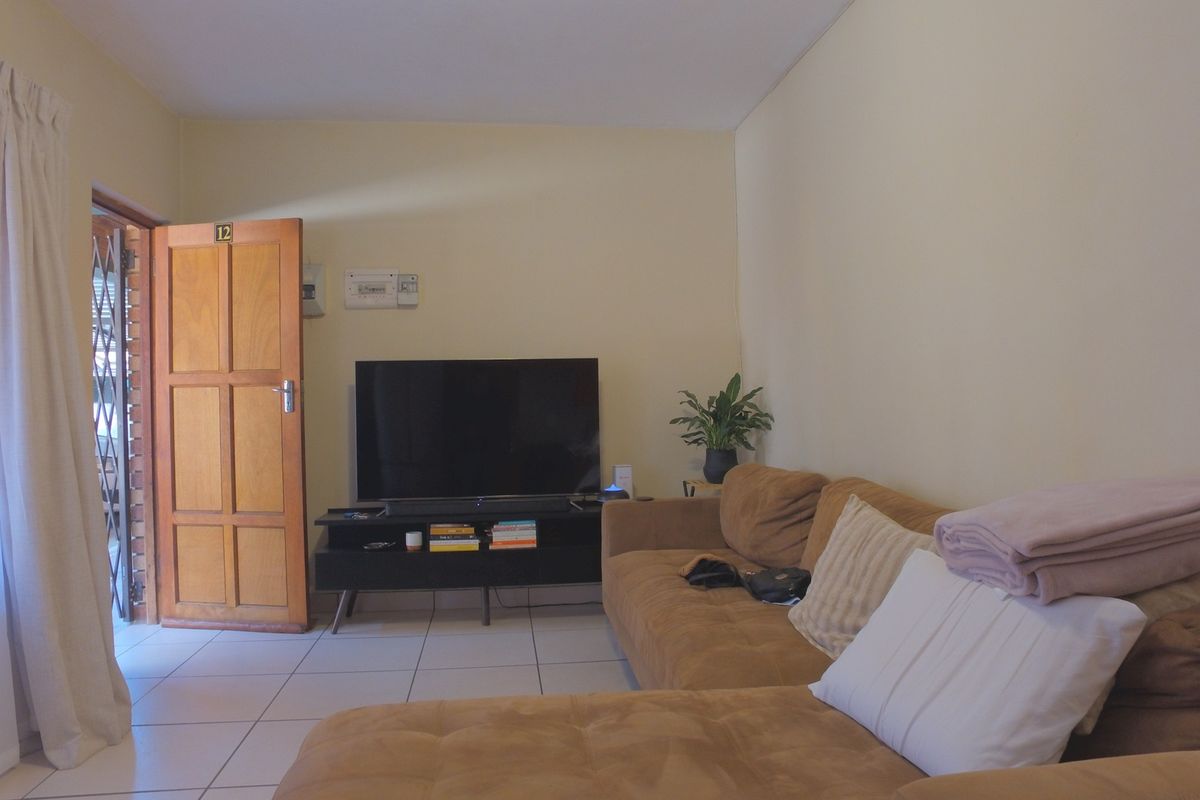 A living room featuring tiled flooring, a timber entrance door with security gate, and a wall-mounted electrical distribution board.