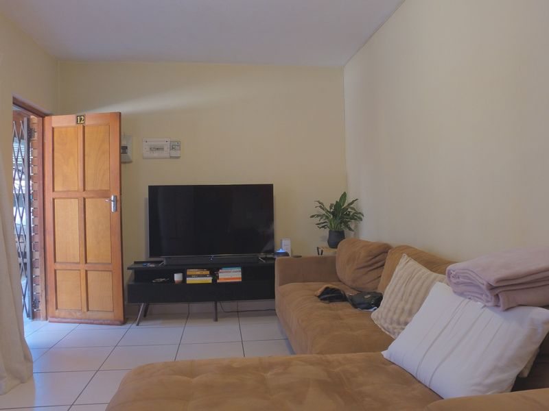A living room featuring tiled flooring, a timber entrance door with security gate, and a wall-mounted electrical distribution board.