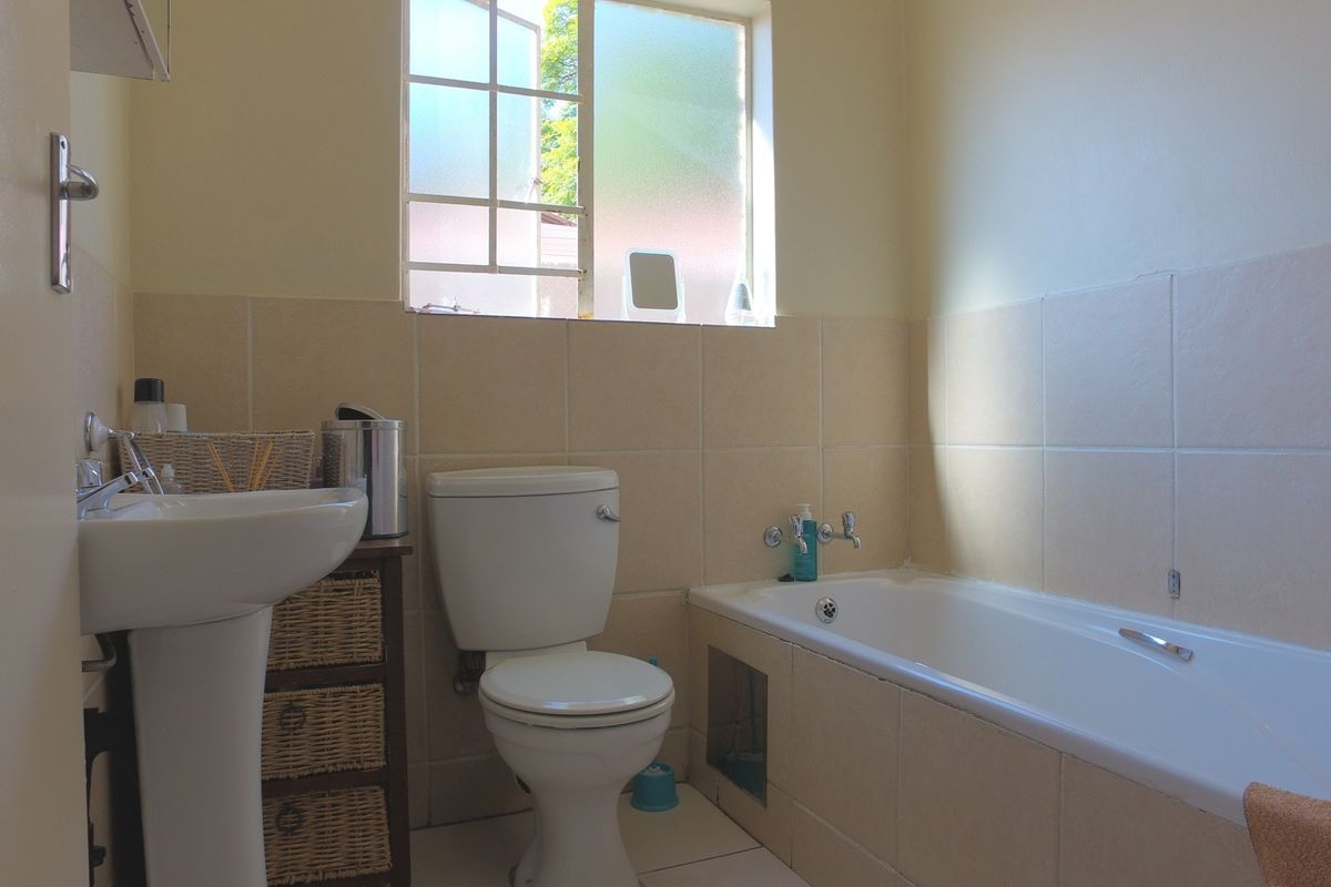 A functional bathroom featuring a pedestal basin, toilet, and bathtub with tiled surrounds and natural light from a casement window.