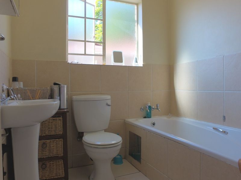 A functional bathroom featuring a pedestal basin, toilet, and bathtub with tiled surrounds and natural light from a casement window.