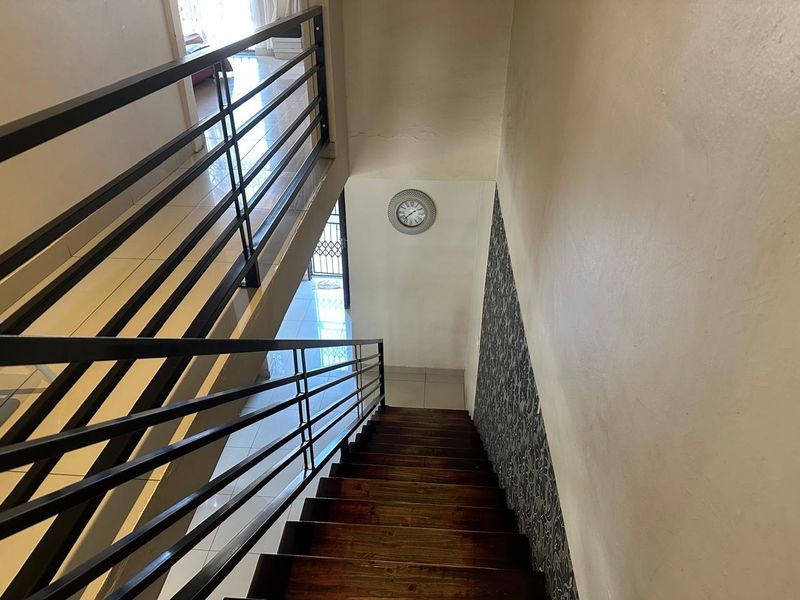 A staircase featuring wooden treads and a modern metal balustrade, leading down to a tiled landing area with decorative wallpaper.