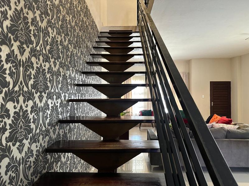 A modern open-tread timber staircase with a sleek metal balustrade, set against a feature wall with decorative patterned wallpaper.