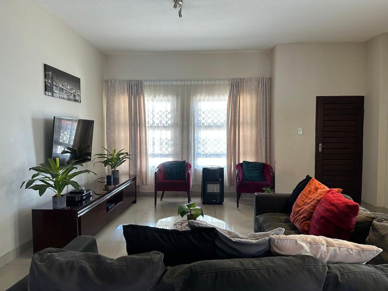 A comfortable living room featuring tiled flooring, large windows with security bars, and a solid wood door, providing a functional and well-lit space.