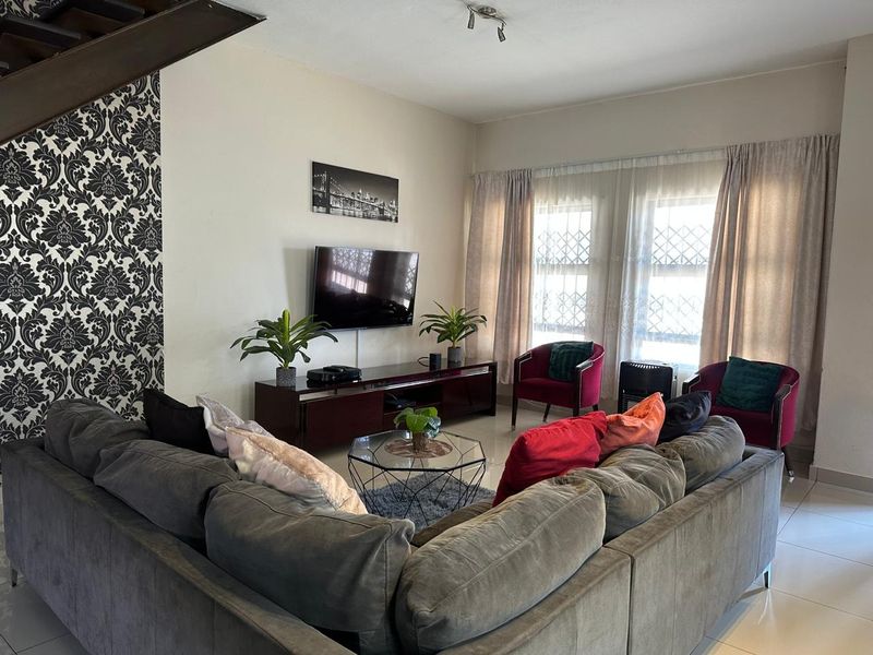A comfortable living room featuring tiled flooring, large windows with security gates, and an adjacent staircase leading to the upper level.