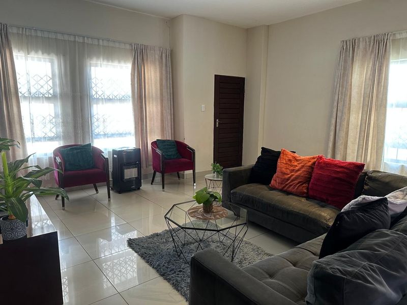 A bright living room featuring large windows with security bars, neutral wall finishes, and polished floor tiles.