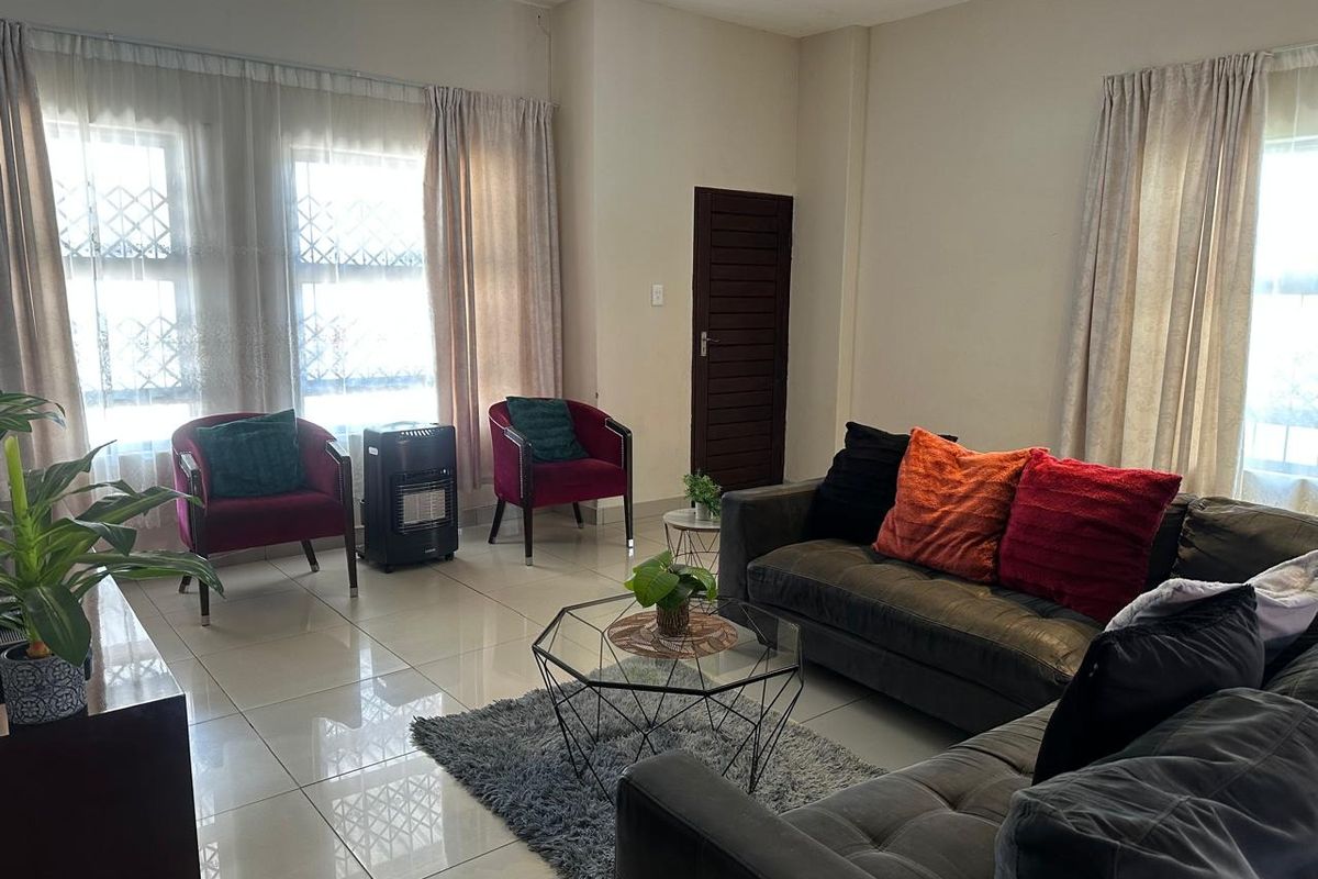 A bright living room featuring large windows with security bars, neutral wall finishes, and polished floor tiles.