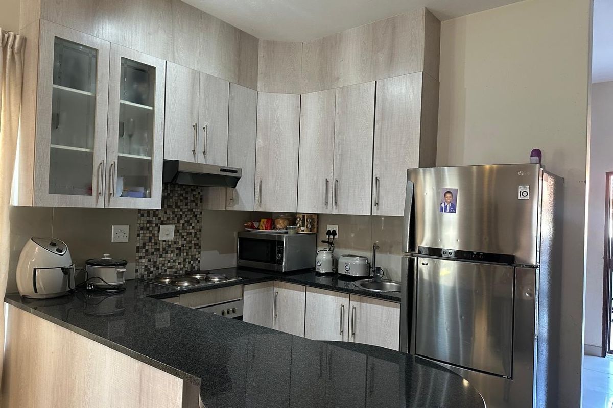 A functional kitchen featuring light wood-grain cabinetry, dark granite countertops, a mosaic tile backsplash, and integrated appliances including a hob and oven.