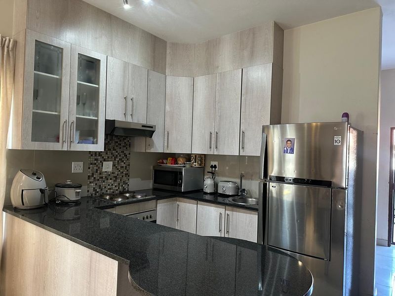 A functional kitchen featuring light wood-grain cabinetry, dark granite countertops, a mosaic tile backsplash, and integrated appliances including a hob and oven.