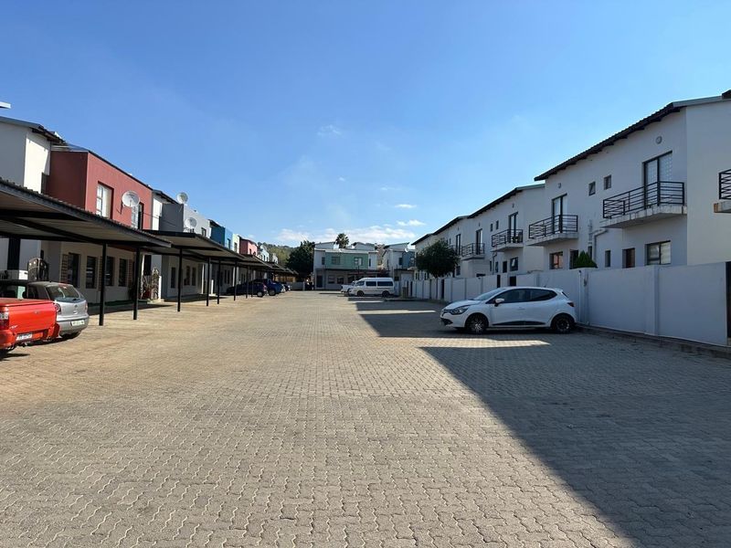 A view of the townhouse complex driveway featuring paved parking areas, covered carports, and multi-story residential units with balconies.