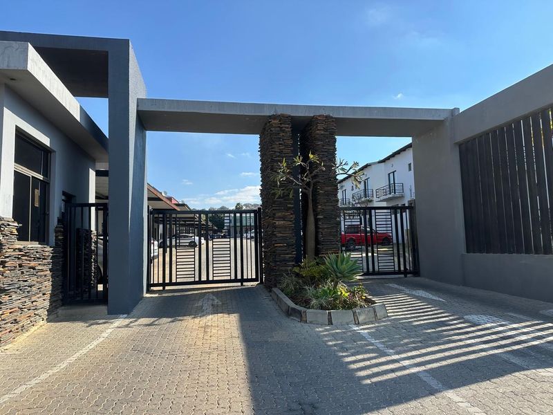 A secure gated entrance to the townhouse complex featuring modern stone cladding, concrete architectural elements, and a paved driveway.