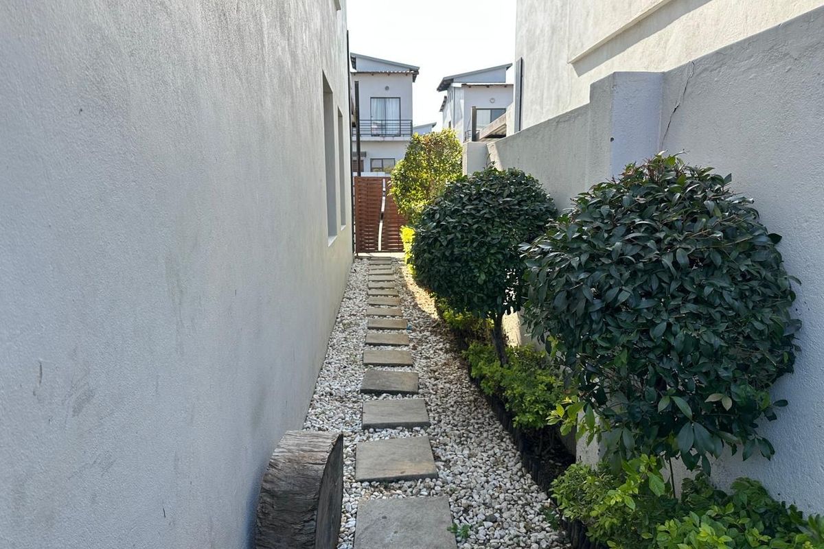 A narrow side passage featuring a stone stepping-stone path set in gravel, bordered by a boundary wall and established shrubs.
