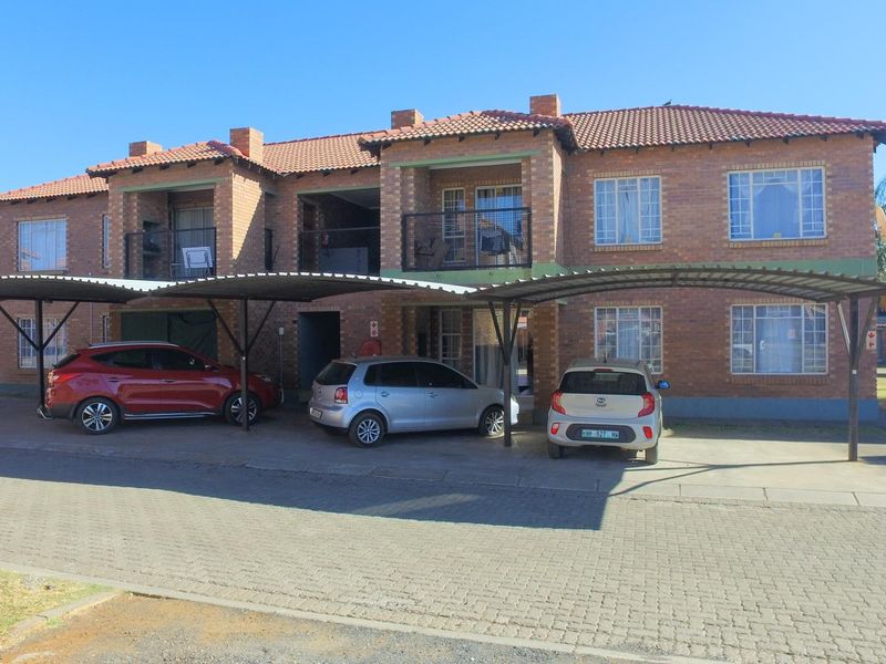 Front view of a two-story brick apartment complex featuring covered carports, balconies, and a paved driveway area.