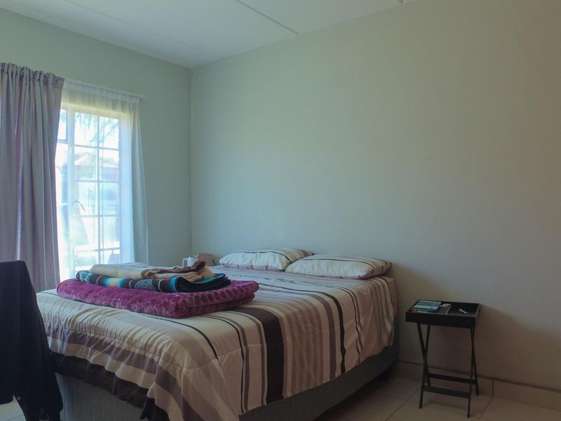 A functional bedroom featuring tiled flooring, a built-in cupboard, and a sliding door providing natural light.