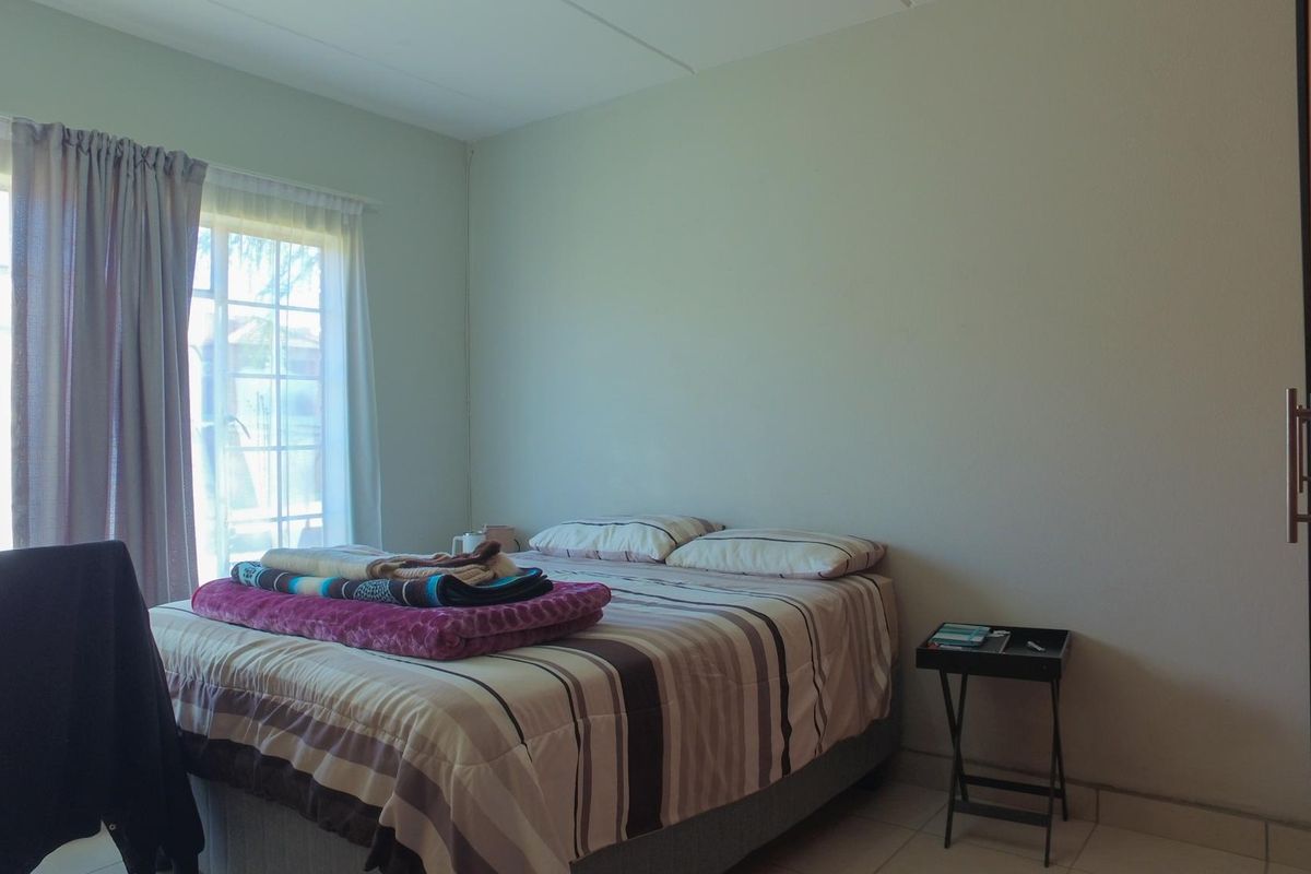 A functional bedroom featuring tiled flooring, a built-in cupboard, and a sliding door providing natural light.