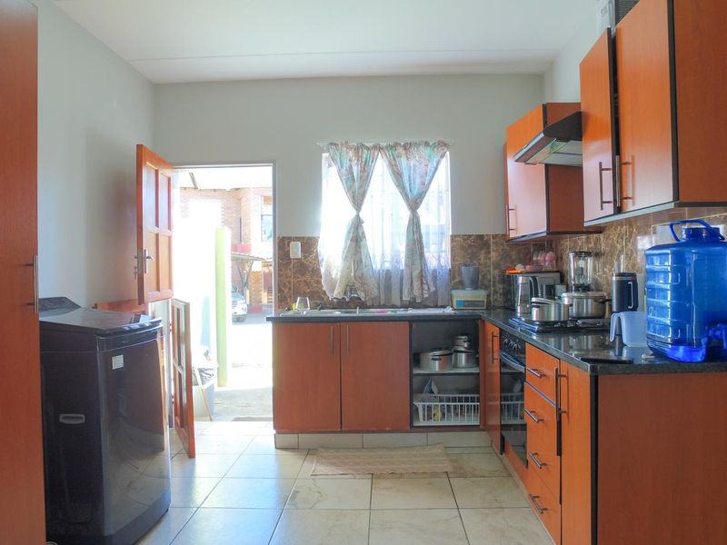 A functional kitchen featuring wood-finish cabinetry, dark countertops, built-in oven and hob, tiled flooring, and direct access to the exterior.