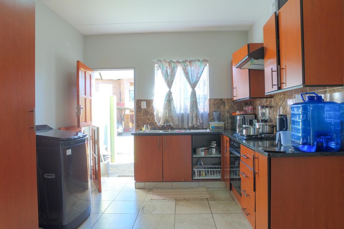 A functional kitchen featuring wood-finish cabinetry, dark countertops, built-in oven and hob, tiled flooring, and direct access to the exterior.