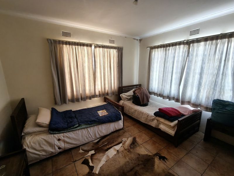 A bedroom featuring tiled flooring and dual windows with curtain rails. Note visible water staining on the ceiling corner requiring attention.