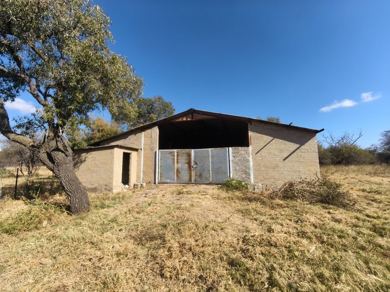 A rustic farm outbuilding featuring masonry walls, a corrugated metal roof, and a large metal gate, set within a rural landscape.