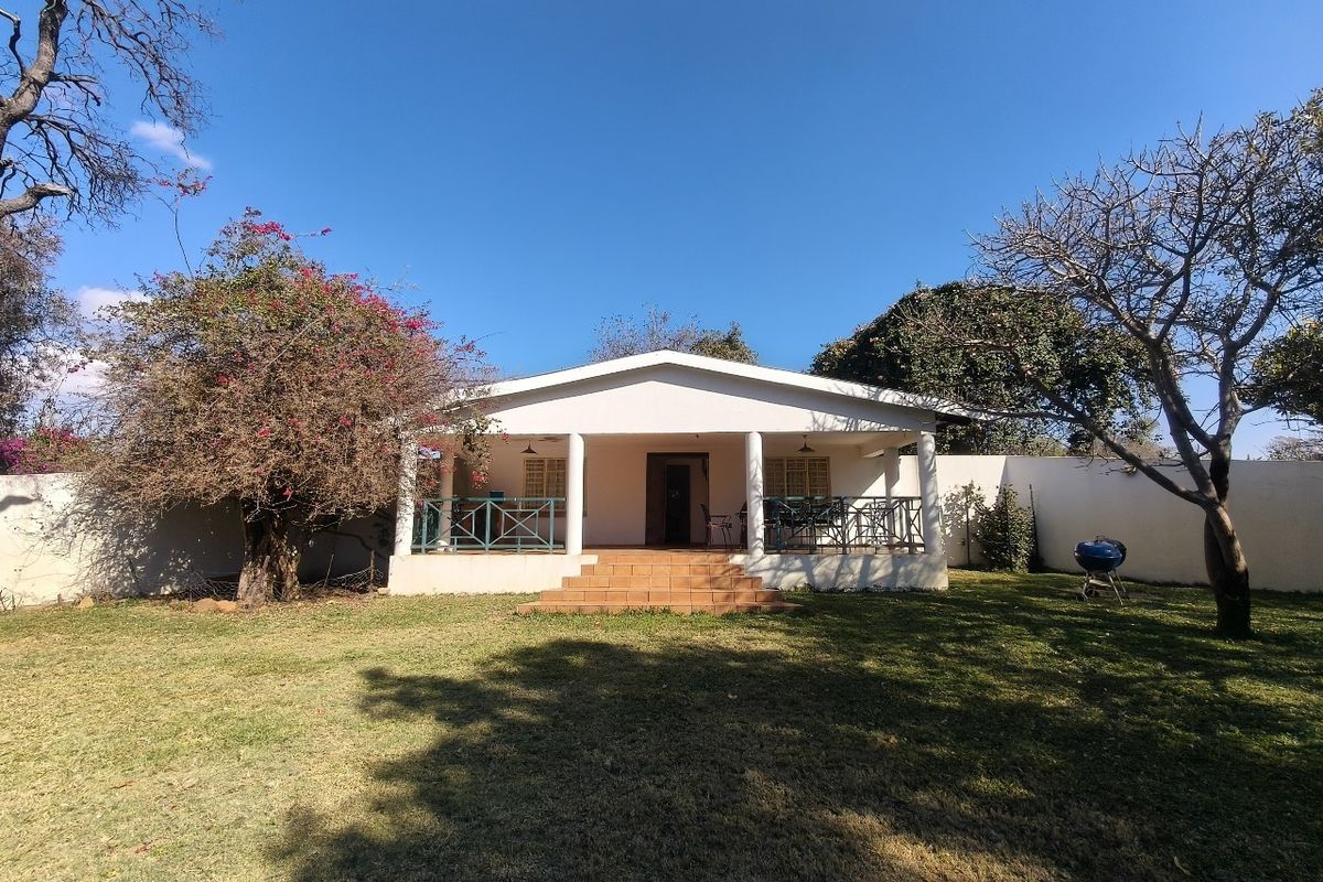 A rear view of the farm house featuring a covered patio with tiled steps, set within a spacious garden with perimeter walling.