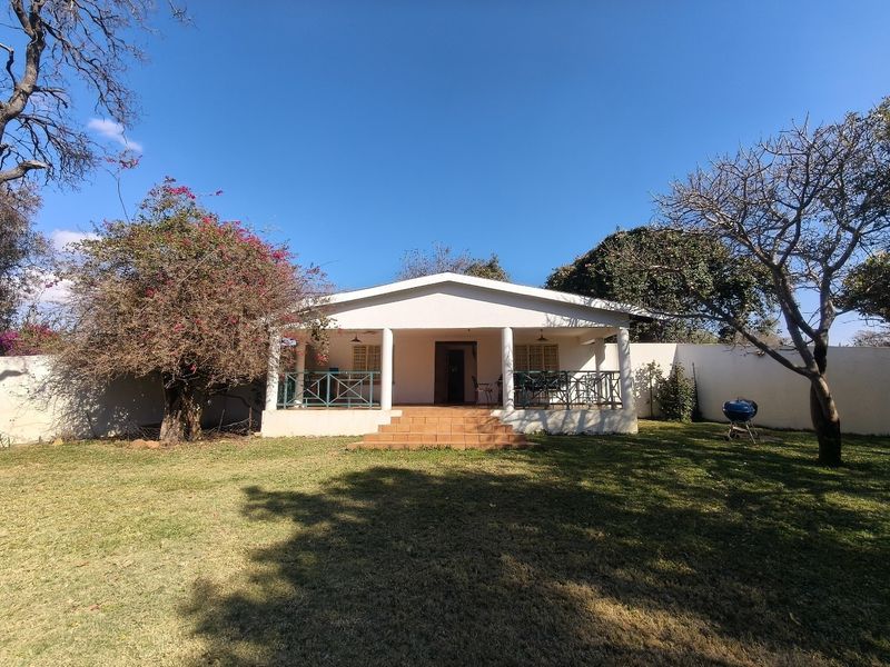A rear view of the farm house featuring a covered patio with tiled steps, set within a spacious garden with perimeter walling.