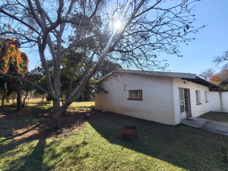 A view of the rear exterior of the farm dwelling, featuring a simple facade, security gate, and surrounding garden area.