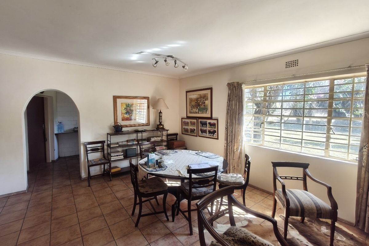 A dining room featuring tiled flooring, an arched entryway, and a large window with security bars, providing natural light and views of the garden.