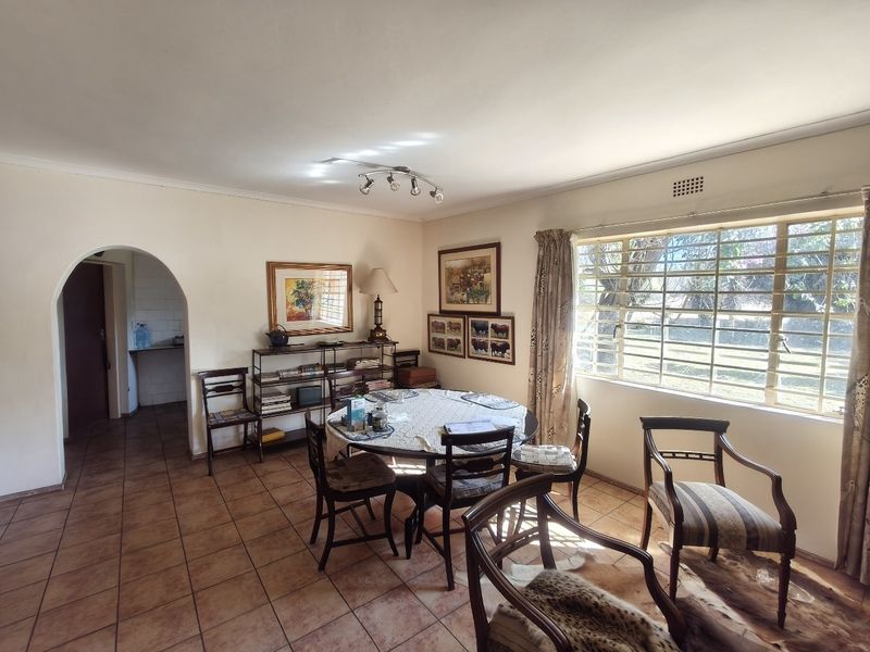 A dining room featuring tiled flooring, an arched entryway, and a large window with security bars, providing natural light and views of the garden.
