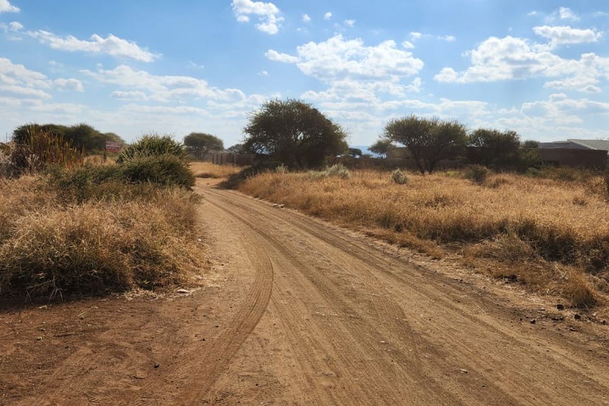 A view of an unpaved access road leading through a vacant residential plot with native vegetation and surrounding landscape.