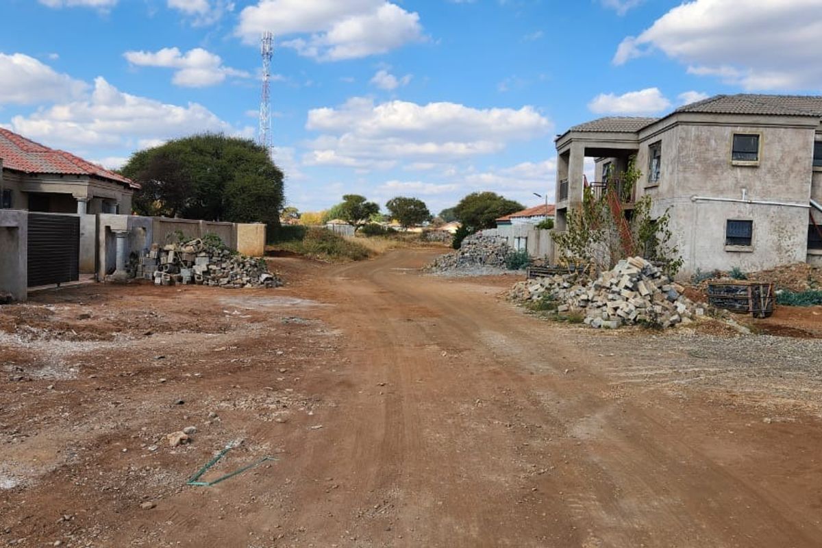 A view of an unpaved residential street featuring surrounding properties under construction and scattered building materials.