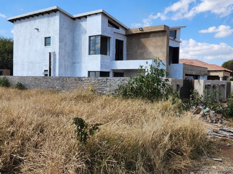 A partially constructed residential property featuring a modern architectural design, brick boundary wall, and an installed water storage tank on a large plot.