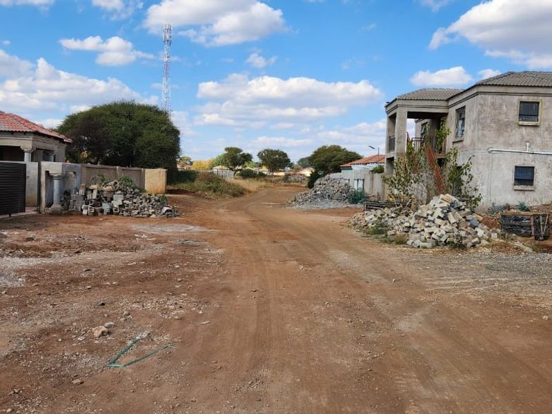 A view of an unpaved residential street featuring surrounding properties under construction and scattered building materials.