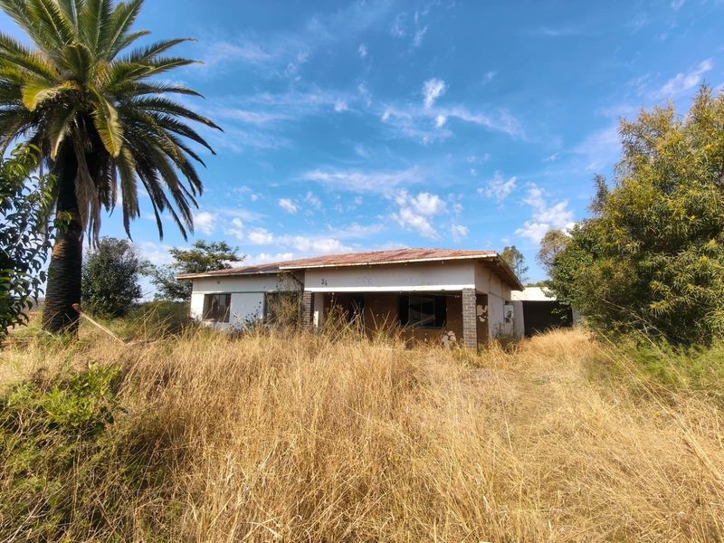 Front view of a dilapidated single-story house featuring a rusted metal roof, overgrown grounds, and significant exterior wear requiring extensive renovation.