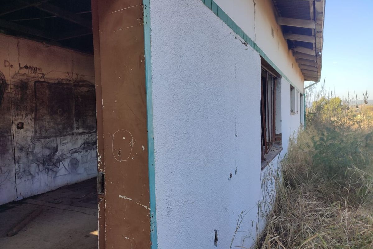 Exterior view of a dilapidated structure showing significant wear, cracked walls, damaged window frames, and graffiti, requiring extensive renovation or structural assessment.