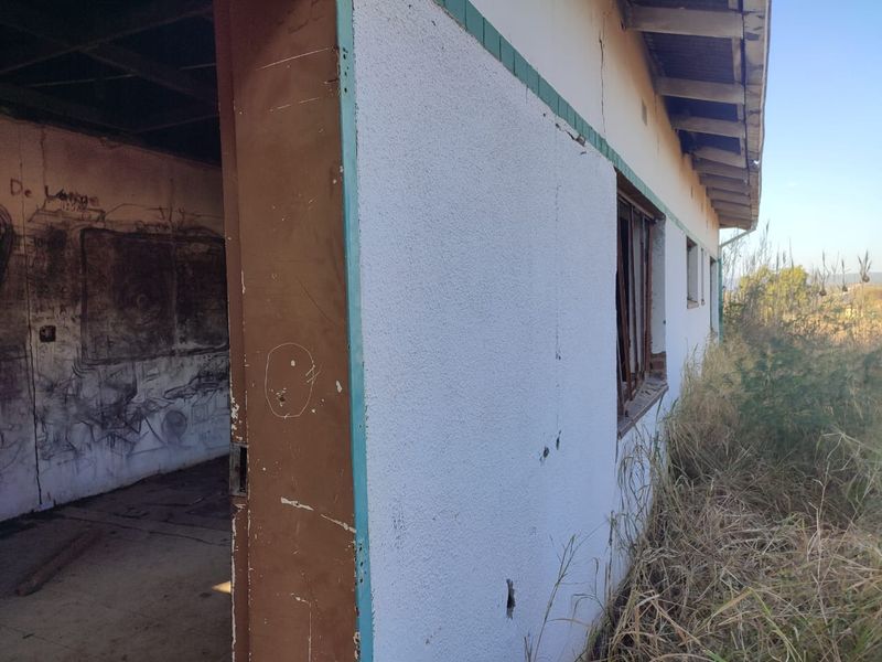 Exterior view of a dilapidated structure showing significant wear, cracked walls, damaged window frames, and graffiti, requiring extensive renovation or structural assessment.