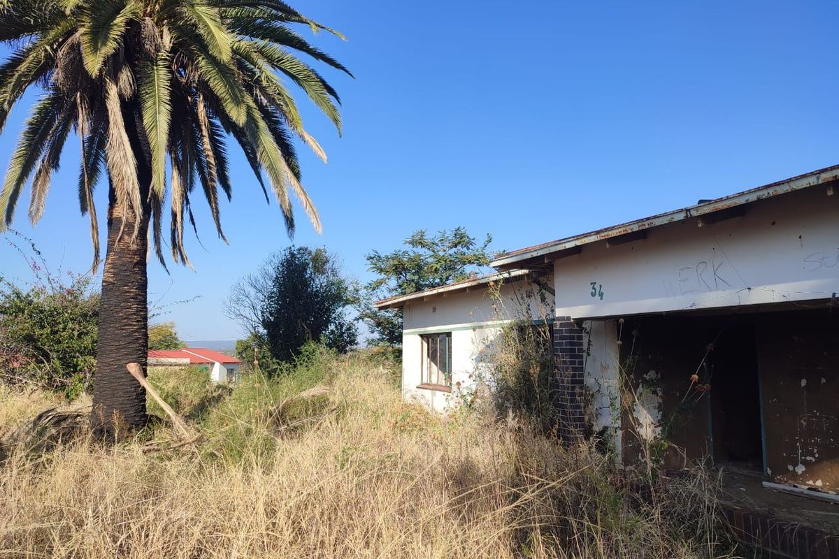 Front exterior view of a property in poor condition, featuring overgrown grounds, peeling paint, and visible graffiti on the building facade.