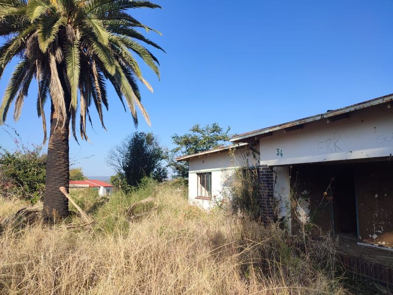 Front exterior view of a property in poor condition, featuring overgrown grounds, peeling paint, and visible graffiti on the building facade.