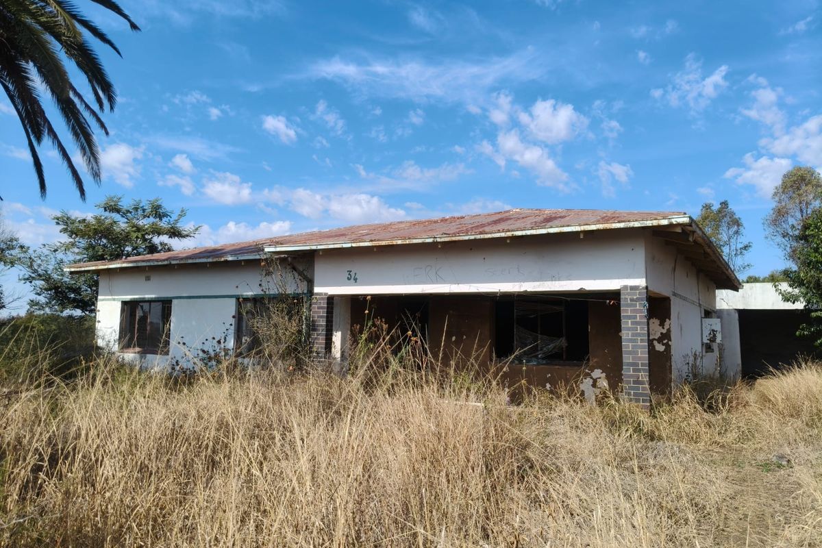 A single-story house in need of significant renovation, featuring a rusted metal roof and overgrown grounds, presenting a major restoration opportunity.
